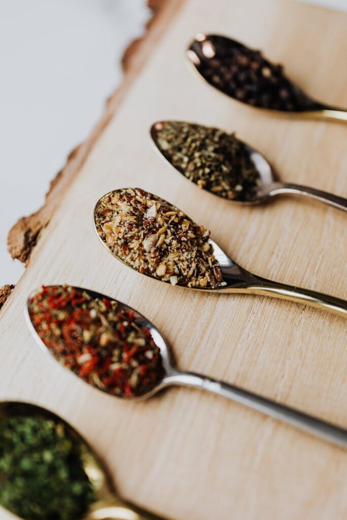 Close-up of assorted herbs and spices in spoons on a wooden board, ideal for culinary themes.